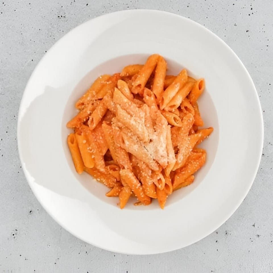 Penne pasta with creamy tomato sauce and grated cheese in a white bowl.