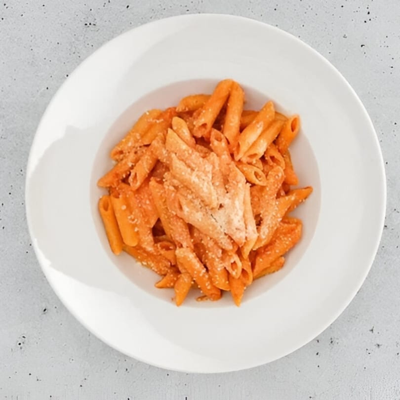 Penne pasta with creamy tomato sauce and grated cheese in a white bowl.