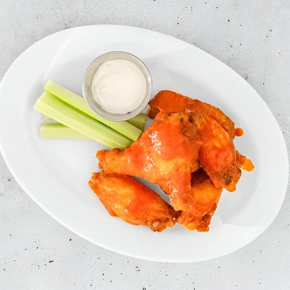 Tita's Pizzeria's buffalo wings, celery sticks, and a small cup of ranch dressing on a white plate.