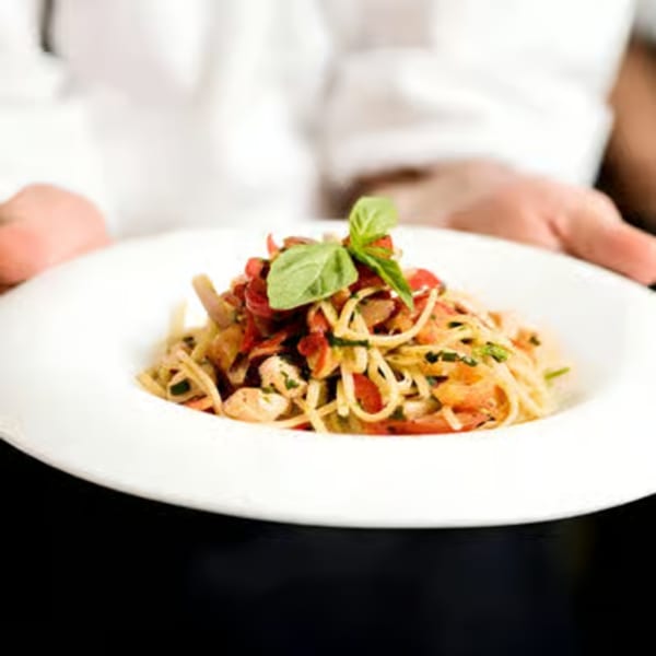 Chef presenting a plate of spaghetti with red sauce, chicken, and basil at Tita's Pizzeria.
