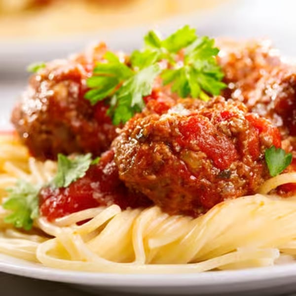 Spaghetti with meatballs, marinara sauce, parsley, and grated cheese on a white plate.